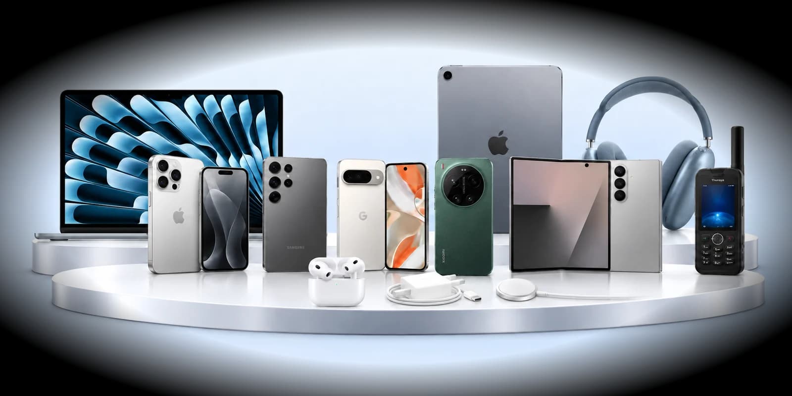 MacBook, iPhone, Galaxy, Pixel, Xiaomi, Galaxy Z Fold, iPad, AirPods, chargers and a Thuraya phone on a white podium